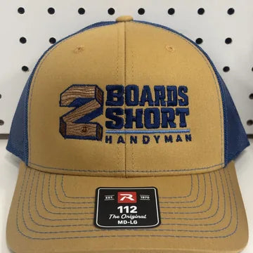Real embroidery proof: a wood-grain number 2 and navy lettering stitched on a gold and royal blue Richardson 112 trucker hat