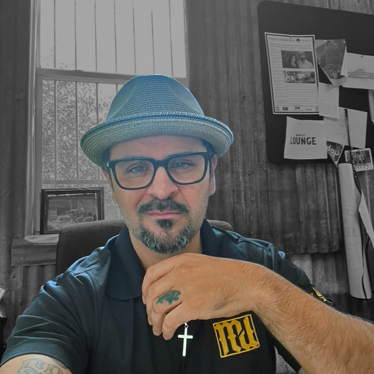 Man in a fedora and glasses wearing a black polo with the gold MyCali Designs logo embroidered on it