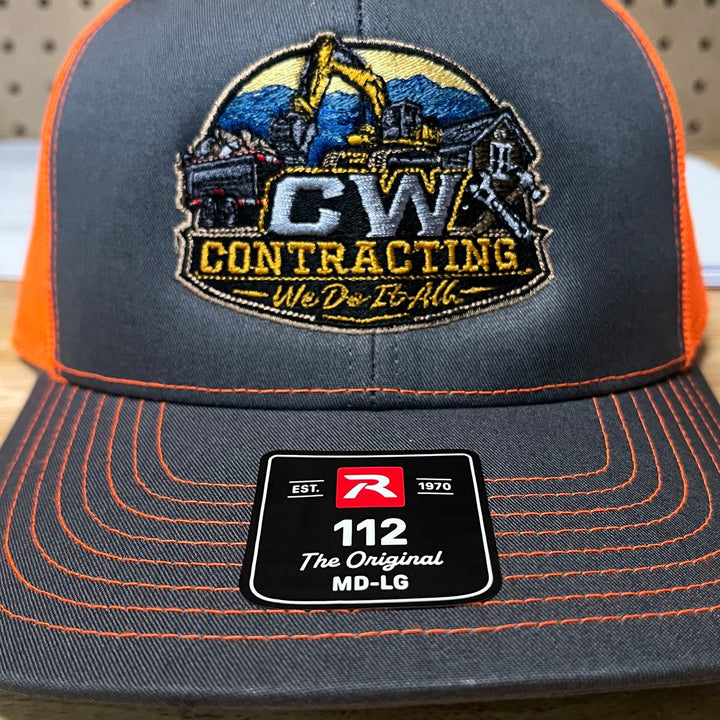 Embroidered excavation contractor logo on a charcoal and orange Richardson 112 trucker hat