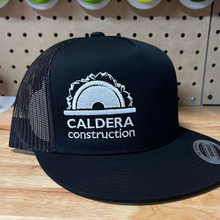 Embroidered construction company logo on a black flat bill trucker snapback