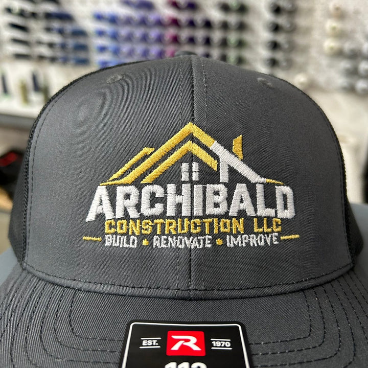 Embroidered construction company logo on a charcoal Richardson 112 trucker hat