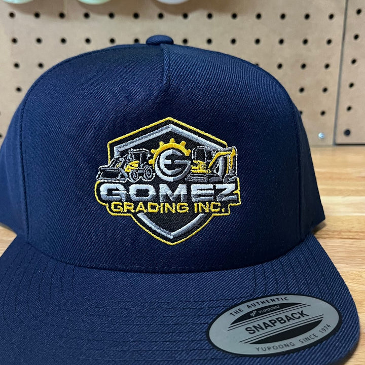Embroidered grading and excavation company logo on a navy flat bill snapback
