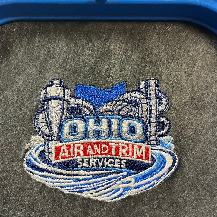 Embroidered air services company logo stitched as a flat sew-out on black backing in the hoop, a real proof before production