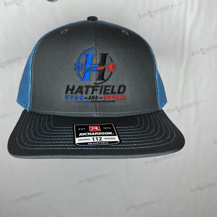 Embroidered HVAC company logo on a charcoal and blue Richardson 112 trucker hat