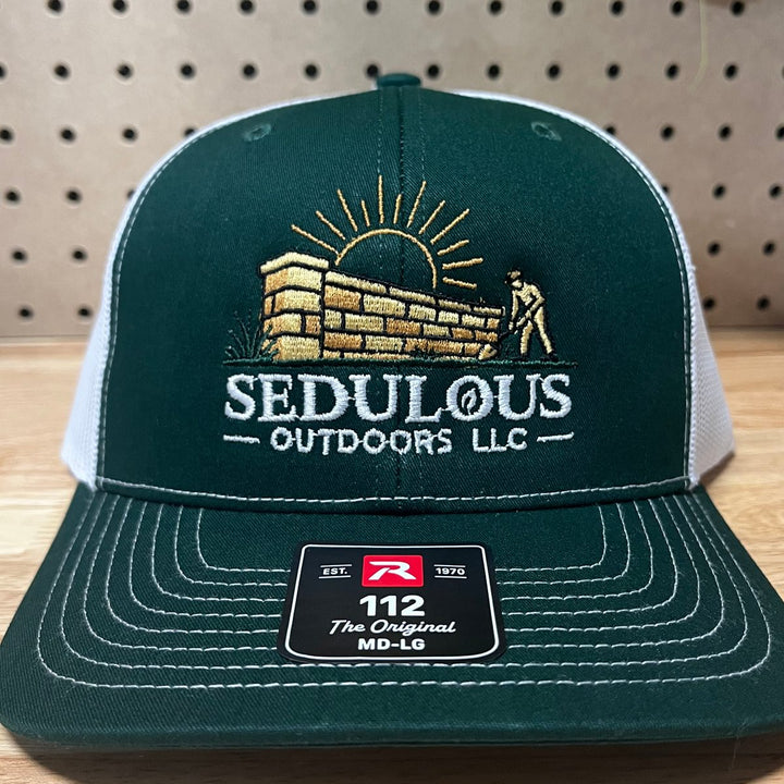 Embroidered hardscape and outdoor company logo on a dark green and white Richardson 112 trucker hat