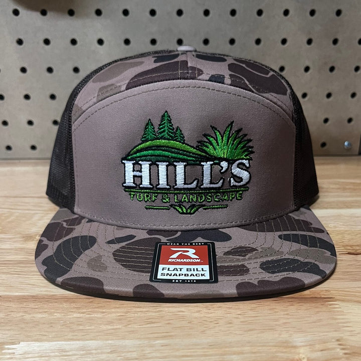 Embroidered turf and landscape company logo on a camo flat bill seven panel snapback