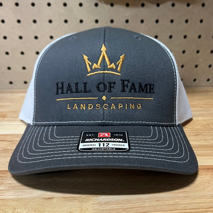 Embroidered landscaping company logo on a slate grey and white Richardson 112 trucker hat