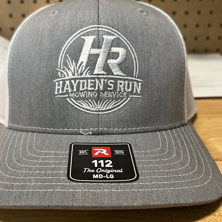 Embroidered mowing service logo on a heather grey and white Richardson 112 trucker hat
