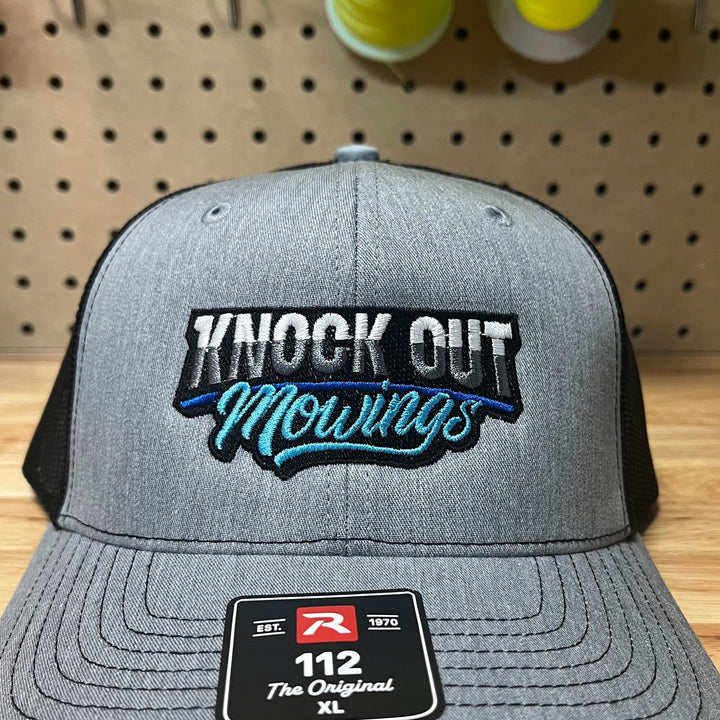 Embroidered mowing company logo on a heather grey and black Richardson 112 trucker hat