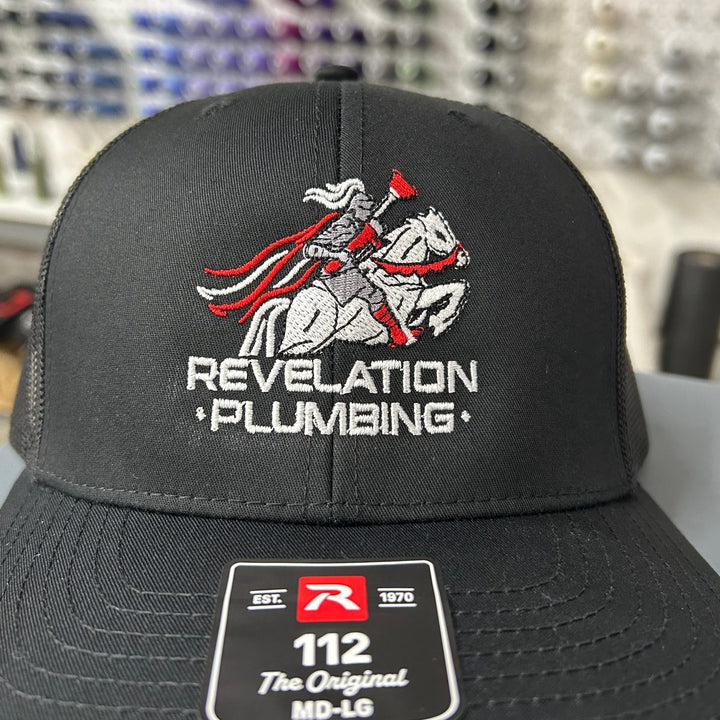 Embroidered plumbing company logo on a black Richardson 112 trucker hat