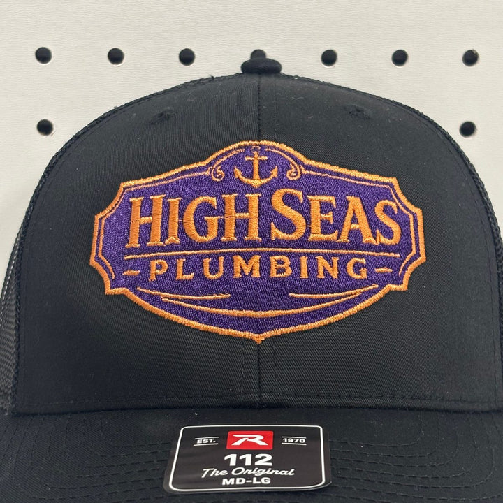 Embroidered plumbing company logo on a black and charcoal Richardson 112 trucker hat