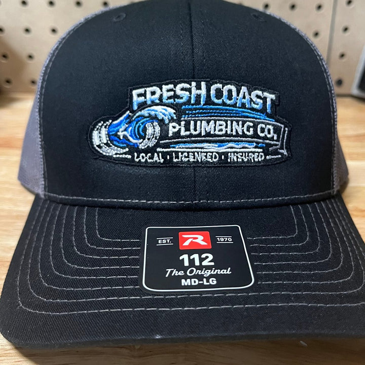 Embroidered plumbing company logo on a black and charcoal Richardson 112 trucker hat