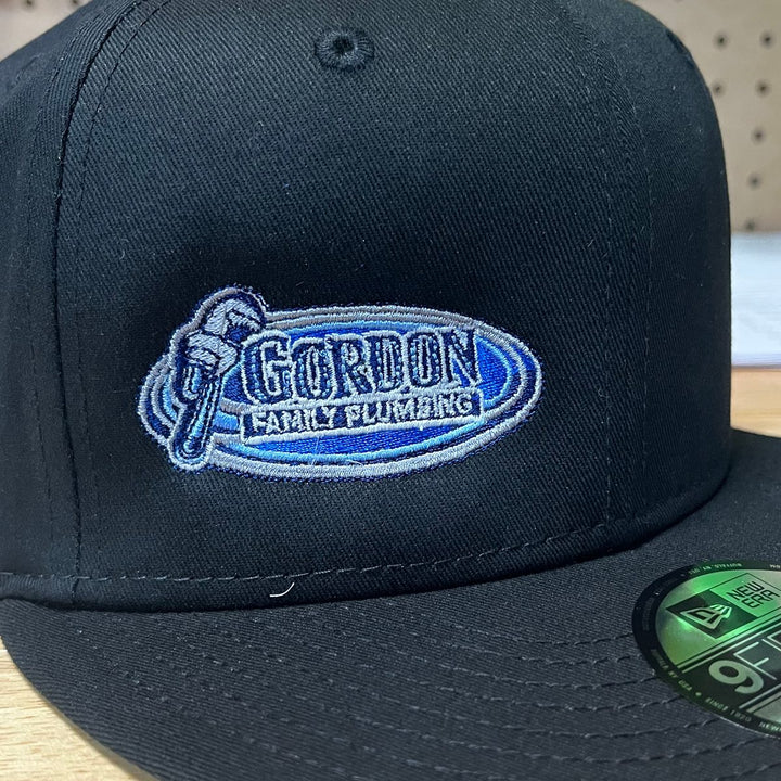 Embroidered family plumbing company logo on a black New Era flat bill snapback